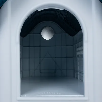 Vnitřní pohled na bílou plastovou psí boudu s ventilační mřížkou na zadní stěně a klenutou střechou.