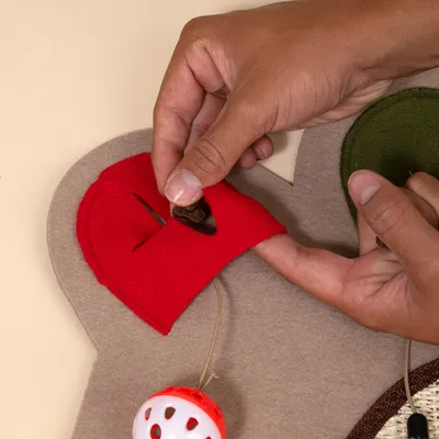 Hand legt ein Leckerli in eine rote Stofftasche auf einer Spielmatte mit integriertem Ballspielzeug.