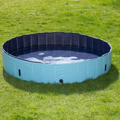 Piscina circular plegable de plástico azul claro, llena de agua, colocada sobre césped. Se observa válvula de drenaje en la parte inferior lateral.