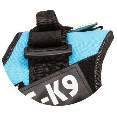 Dettaglio pettorina per cani in tessuto azzurro e nero con scritta visibile '-K9' su etichetta nera, anello metallico e maniglia in nylon.