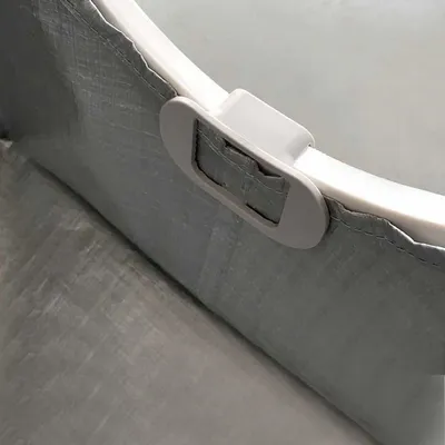 Detail van een grijze kunststof gesp en rand met textiel, zichtbaar stiksel en bevestiging aan een lichtgrijs oppervlak. Materiaal: plastic en stof.