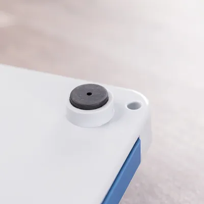 Gros plan sur un coin d’un objet en plastique blanc avec patin antidérapant rond noir et trou visible dans l’angle.