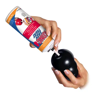 Hand squeezing Kong Easy Treat Paste into a black Kong toy. Instructions for filling the toy with the paste.