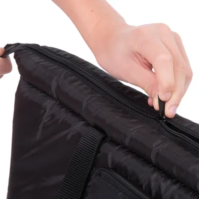 Main ouvrant une fermeture éclair sur un sac ou coussin noir en tissu, poignée visible sur le côté.