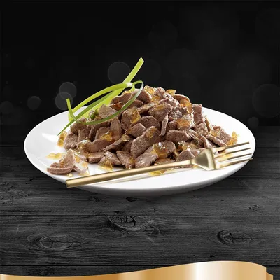 Tallerken med stykker af vådfoder i gelé, pyntet med grønne urter, serveret med gaffel og kniv på sort træbord. Ingen synlige mærker eller tekst.