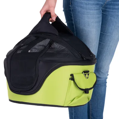 Sac de transport pour animaux, tissu noir et vert avec poche latérale, poignée de transport, parties en maille pour aération, porté à la main par une personne en jean.