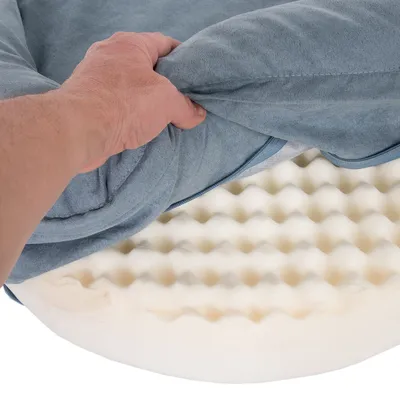 Hånd løfter blå betræk for at vise bølget skumfyld i en hundeseng. Synlig struktur af skummateriale og tekstilbetræk.