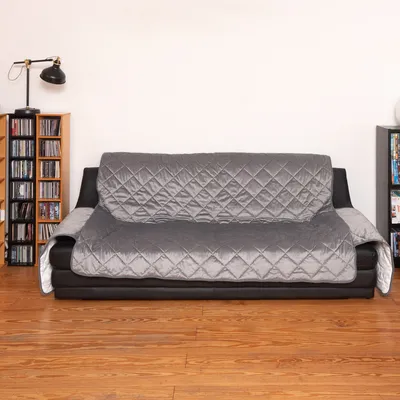 Gesteppter, grauer Sofaschutzbezug aus Stoff auf einem schwarzen Sofa, Bezug bedeckt Sitzfläche, Rückenlehne und Armlehnen.