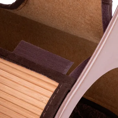 Gros plan sur une fixation en scratch et des matériaux visibles : feutre marron, plastique beige et lattes de bois clair.