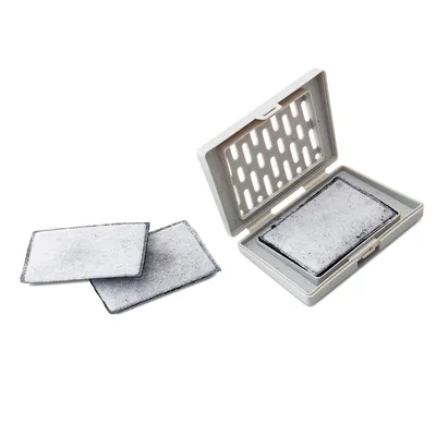 Filtros rectangulares de carbón activo, dos sueltos y uno colocado en un soporte de plástico blanco con tapa abierta. Material visible: plástico y filtro textil.