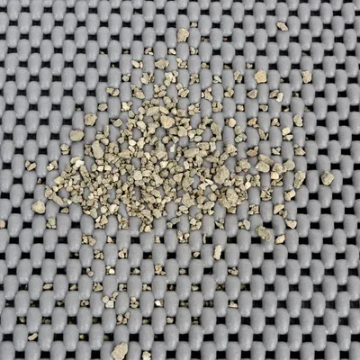 Kattenbakvulling korrels verspreid op een grijze kunststof mat met open structuur, zichtbaar detail van materiaal en formaat van de korrels.