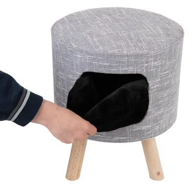 Grauer Hocker mit Holzbeinen und schwarzem, weichem Innenraum. Hand zeigt Zugang zur Öffnung des Hockers.