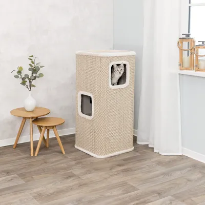 Kratzbaum in beige mit zwei Öffnungen, Katze schaut aus einer Öffnung heraus. Steht neben einem Holztisch und Dekoration im Wohnzimmer.