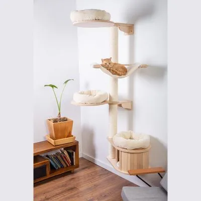 Tiragraffi ad angolo in legno chiaro con quattro piattaforme e letti imbottiti color crema, un gatto arancione sdraiato sull’amaca centrale.