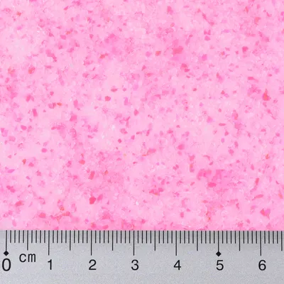 Close-up of pink granules with a centimetre scale, showing particle size and texture.