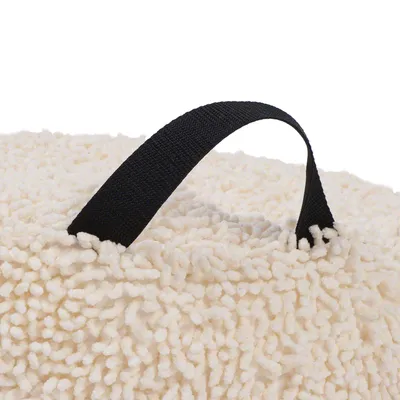 Poignée noire en tissu sur coussin ou panier pour animal, surface beige à texture bouclée type peluche. Aucun texte ni marque visible.