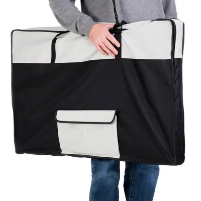 Draagtas van zwart en lichtgrijs textiel met handvatten en voorvak, vastgehouden door persoon in spijkerbroek en grijze trui. Materiaal: stof.