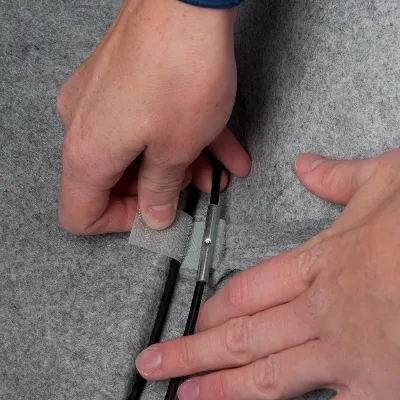 Hände befestigen ein Kabel mit einem Klettverschluss an einer grauen Filzoberfläche.