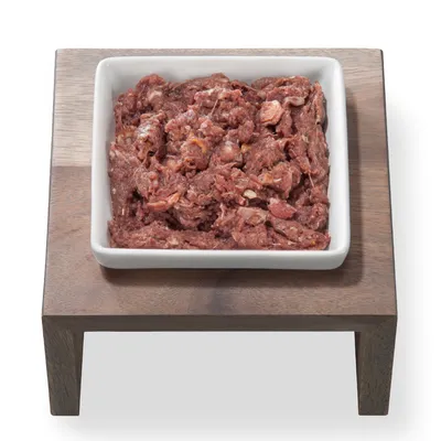 Frisches rohes Fleisch in einer weißen Keramikschale auf einem Holzständer präsentiert.