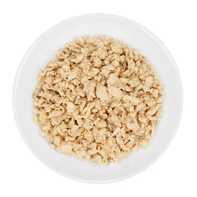 Plato blanco con comida húmeda para mascotas en trozos pequeños de color beige claro, vista cenital. No se muestra marca ni envase.