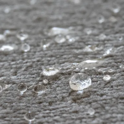 Gros plan sur des gouttes d’eau posées sur une surface textile grise, montrant la texture du tissu et l’effet perlant de l’eau.