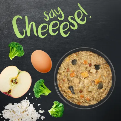 Bowl of food surrounded by broccoli, egg, apple, and cheese with the text 'say cheeese!' above, highlighting visible ingredients in the product.