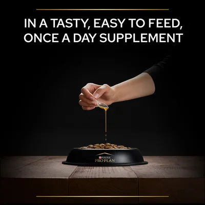 Χέρι ρίχνει υγρό συμπλήρωμα σε ξηρά τροφή σκύλου σε μπολ με το όνομα PURINA PRO PLAN. Κείμενο στα αγγλικά: IN A TASTY, EASY TO FEED, ONCE A DAY SUPPLEMENT.