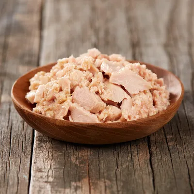 Nahaufnahme von zerkleinertem, rosa Fleisch in einer Holzschale auf einem rustikalen Holztisch. Produktabbildung für Tiernahrung.
